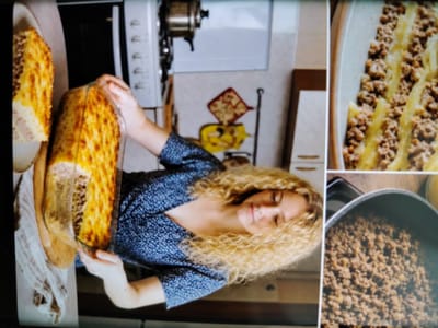 A woman with curly blonde hair, wearing a dark blue patterned dress, is holding a rectangular glass baking dish containing a golden-brown baked dish with a meat filling. To the left of the baking dish, another similar dish is partially visible. In the background, a kitchen is visible with appliances and utensils. To the right of the woman, a close-up view shows a casserole dish filled with pasta and meat sauce, and below that, a pot filled with cooked ground meat. The scene appears to be indoors, likely in a home kitchen. There is no information within the image to suggest the location is the city of Gyumri, Armenia.