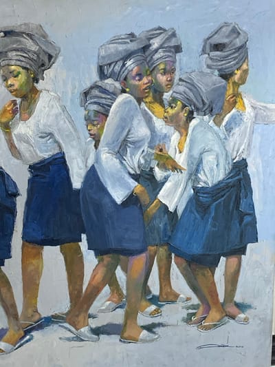 This oil painting depicts a dynamic group of seven adult females, ostensibly within the city of Ikate, Nigeria, arranged in a walking formation. Each individual has dark skin with artistic highlights in green and yellow tones on their faces, and is adorned with a large, intricately tied grey headwrap (gele). They wear long-sleeved white blouses and knee-length blue skirts. Footwear comprises simple white flat sandals or slippers. Several women wear golden hoop earrings, and one on the far left has a golden bangle on her wrist.
In the mid-ground, a woman positioned slightly right of center holds a small, light-colored rectangular object in her right hand while making a gesture with her left, appearing to communicate with the woman immediately to her right. Another woman, positioned to the far left, looks downward. The figures are closely spaced, implying a procession or close-knit group. The environment consists of a textured, light blue-grey background and a light grey ground plane, suggesting an open, undefined setting. Visible brushstrokes are present throughout the composition. A signature and the year "2010" are located in the lower right corner.