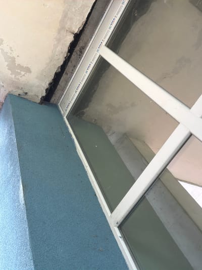 An interior view showing a white-framed skylight above a wall, possibly in Dolna Mitropolia, Bulgaria. The wall is textured blue, while the adjacent wall is peeling and grey. Visible above is the window and parts of the ceiling in varying shades of gray.