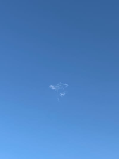 A single, wispy cloud is visible against a clear blue sky. The cloud is small and irregularly shaped, appearing somewhat like a question mark or a distorted heart. There are no other discernible objects or features in the image. The setting is an outdoor environment.