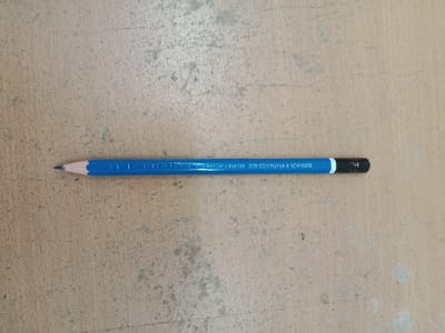The image shows a blue pencil lying horizontally on a brown surface. The pencil has a black eraser on one end and a sharpened point on the other. The pencil has the words "FOR COMPUTER & SCANNER" printed on it.  It is difficult to determine the exact location in Kecamatan Ngaliyan, Indonesia, using only the coordinates provided. It is likely an indoor setting.