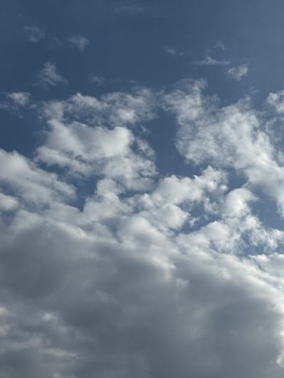 The image displays an outdoor atmospheric scene, reportedly captured in Stalden (VS), Switzerland. The upper portion of the frame features a clear, medium-blue sky interspersed with multiple scattered, white, irregularly shaped cumulus clouds of varying sizes. Below this, a denser, thicker layer of dark grey clouds occupies the lower half to two-thirds of the frame, obscuring the sky beneath. The transition between the brighter, white clouds and the darker, lower cloud layer is gradual, with some white clouds appearing above the grey mass. No human figures, terrestrial objects, or specific geographical features are visible within the frame. The scene depicts only sky and clouds, with no discernible actions or interactions occurring.