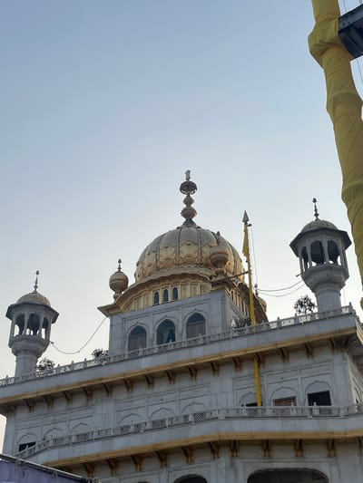 The image shows a close-up view of the Golden Temple in Amritsar, India. The temple's iconic golden domes and white marble facade are visible against a clear sky. There are no people or animals in the frame, and no discernible actions or interactions are taking place. The environment appears to be calm and serene. The image is taken from a slightly upward angle, highlighting the architectural grandeur of the sacred Sikh site.