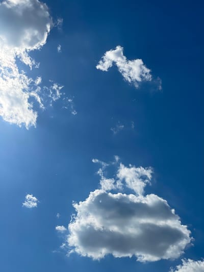 This media file captures a bright, clear blue sky with scattered white cumulus clouds. The clouds vary in size and density, with some appearing wispy and others more substantial. One large, imposing cloud dominates the upper right quadrant of the image, casting shadows that give it a three-dimensional appearance. Smaller, scattered clouds are visible throughout the frame, some appearing like delicate brushstrokes against the vast expanse of blue. The lighting suggests it is daytime, likely midday or early afternoon, given the brightness and the shadows on the larger cloud. There are no visible people, objects, text, or specific location cues to indicate an activity or event. The overall impression is one of a serene and open sky, characteristic of fair weather. The location context is Syrnyky, Ukraine, which provides a geographical setting for this otherwise generic sky scene.