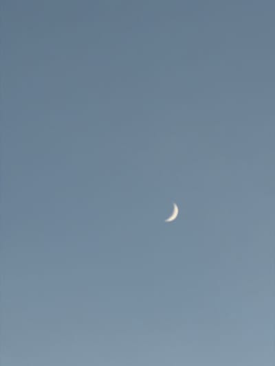 A crescent moon is visible in a pale blue sky. The image is a vertical, full-frame shot of the sky with no discernable landmarks or features from New Westminster, Canada. There are no people or objects present in the image. The environment is entirely the sky.