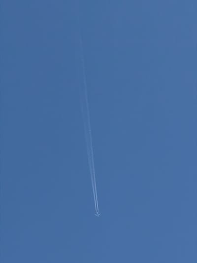 A distant commercial jet flies across a clear blue sky, leaving a white contrail in its wake. The plane is silhouetted against the sky and angled slightly downward. The location is likely Pentre, United Kingdom, as requested. The scene depicts a high-altitude aviation event with no observable human activity or terrestrial elements.
