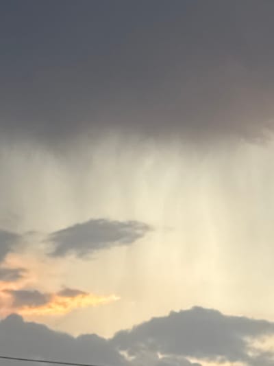 The image shows a sky scene. The sky transitions from dark gray clouds on the left to brighter, yellowish-white clouds on the right. There's a vertical formation of darker clouds in the center, and near the right edge, a patch of clouds is illuminated with an orange-yellow glow. Thin dark lines appear near the rightmost edge. The location, Pchelnik, Bulgaria, is not visibly represented in the image.