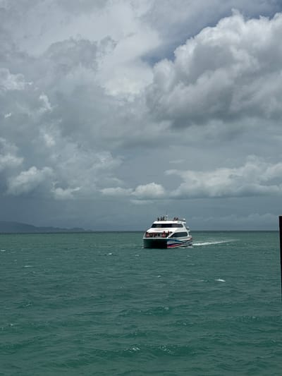 A ferry travels across the water under a cloudy sky. It is likely near Thong Sala, Thailand, given the prompt.