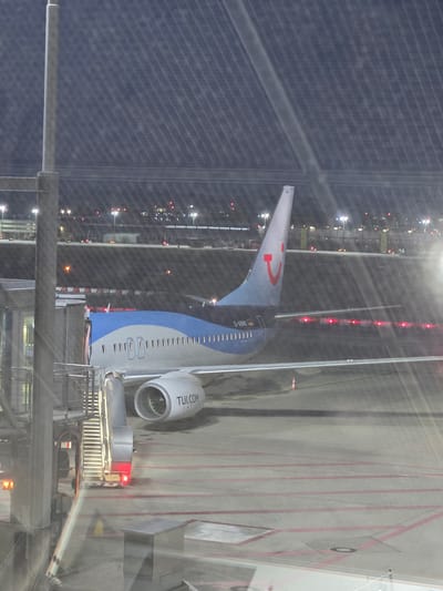 An airplane, identified by the livery "TUI.COM" and registration "D-ABWO", is parked at night on the tarmac at Stuttgart Airport (STR) in Echterdingen, Germany. The aircraft, a Boeing 737-800, has its boarding stairs attached to the front fuselage. The scene is illuminated by various airport lights and the lights from the terminal building in the background. The airport's distinctive diamond-patterned roof structure is visible overhead. The tarmac is marked with red lines.