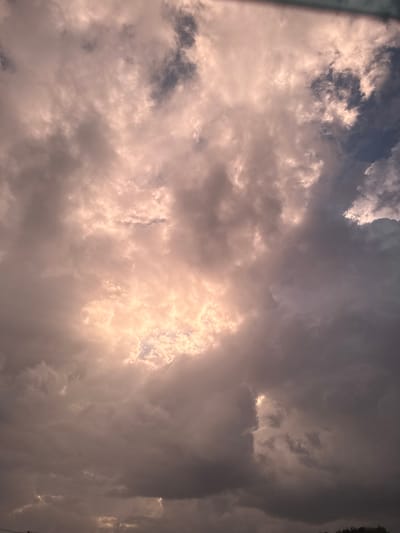 The image shows a sky filled with dramatic, stormy clouds. The clouds are dark and heavy, with patches of bright, warm light breaking through in the center. The light creates a halo-like effect, illuminating some of the smaller clouds within the larger mass. The overall impression is one of a powerful, dynamic weather event. The image does not contain any specific details that would allow for its location to be determined within the city of Berezniki, Russia. There are no people, identifiable landmarks, or any other contextual clues present in the scene. The image is a close-up view of the sky.
