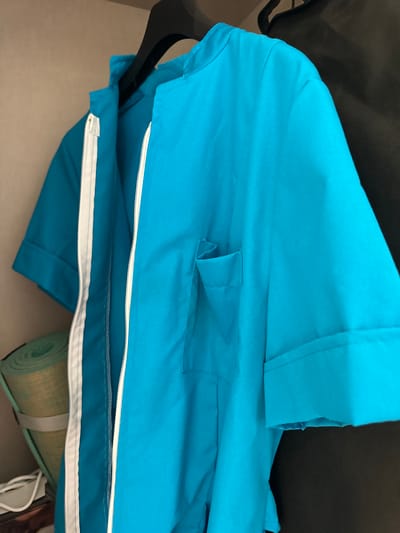 The image shows a close-up of a bright blue garment, likely a jacket or a shirt, with a white zipper running down the front. The garment is laid out on a surface, with a black hanger visible on the left side, suggesting it's being prepared for storage or transport. A rolled-up mat, possibly a yoga or sleeping mat, in a light green color with a beige textured surface, is partially visible at the bottom right. The background is dark and out of focus, creating a shallow depth of field that emphasizes the blue garment. The lighting is even, suggesting an indoor setting. No people are visible in the image. The overall impression is one of a practical, everyday item, possibly packed for a trip or outing. The context of Murcia, Spain, does not provide any specific visual cues within the image itself.