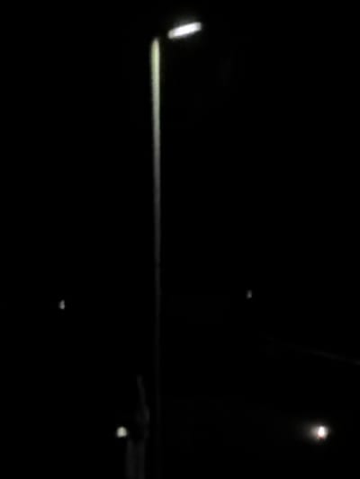 The image appears to be taken at night. A horizontal light source illuminates what may be a road surface or railing. Another light source is visible in the upper right. A darker object is visible in the lower right with a smaller light source underneath. There is no information in the image to verify location in Sant Martí Sarroca, Spain. The lack of detail makes it impossible to identify any people or discern any interactions.