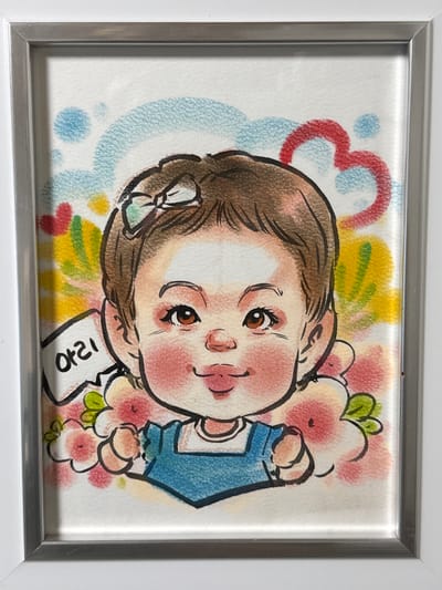 A framed watercolor painting depicts a stylized, cartoonish portrait of a baby. The baby has a round face with rosy cheeks, large brown eyes, and a small smile. They have brown hair with a white bow on top and are wearing a blue overall-like garment. The background is colorful, with soft blue and red cloud-like shapes, and yellow and green floral elements. A small white tag with Korean characters, "아기" (meaning "baby"), is attached to the baby's ear area. The painting is enclosed in a silver frame. The image appears to be a personal artwork, possibly a gift or memento, and does not depict any specific identifiable landmarks or locations within Gwangju, South Korea.
