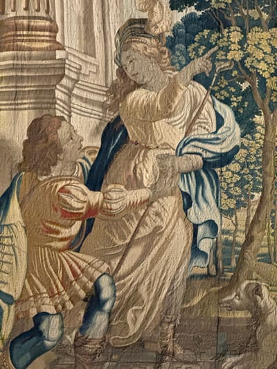 This tapestry depicts a scene with multiple figures in what appears to be an outdoor setting, possibly a garden or forest, suggested by the lush foliage and trees in the upper left. Two prominent figures, a woman and a man, are central to the composition. The woman, in the upper part of the image, is dressed in flowing garments of white and blue and holds a staff or rod. Her head is turned, and her expression is difficult to discern clearly due to the tapestry's texture and detail. She seems to be in motion, perhaps gesturing or walking.
Below and to the right of the woman lies a man, also richly dressed in attire that includes striped fabric, red accents, and blue leg coverings. He appears to be either lying down or wounded, with his head turned to the side. His posture suggests a state of repose or vulnerability. In the lower left, architectural elements resembling steps or platforms are visible, rendered in muted tones. The overall color palette is dominated by earthy browns, blues, greens, and creams, typical of historical tapestries. The lighting seems subdued, consistent with an indoor or shaded outdoor environment. There is no visible text in the image. The scene evokes a narrative, possibly from mythology, history, or a religious story, though the specific event or context is not explicitly clear from the visual information alone. The style suggests a Renaissance or Baroque period of art. The location context of Santiago de Compostela, Spain, might suggest a connection to a pilgrimage or a historical event relevant to the region, but this is not directly represented in the tapestry itself.