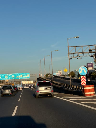 The image shows a traffic jam on a highway in Boulogne Sur Mer, Argentina. The sky is blue and clear. Multiple cars are visible in the jam. Road signs are visible. A light blue sign on the side of the road reads "Use su carril". A blue sign with a white arrow split into two directions, left and right, is also present.