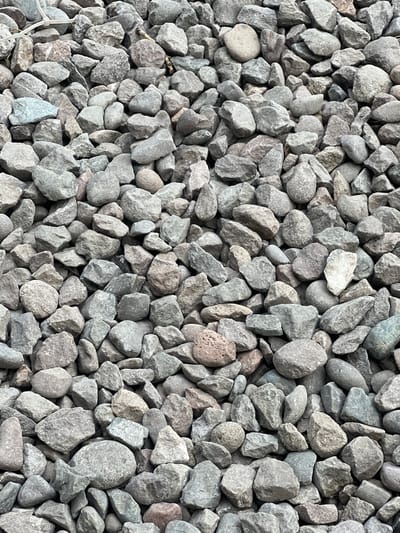 The image shows a pile of gray, rough-textured gravel. The stones are of various sizes and shapes, from small pebbles to larger rocks. Some of the stones have smooth, rounded edges, while others are jagged and angular. The gravel is dry and dusty, and there are no signs of water or vegetation. The image is taken from a close-up perspective, and the gravel fills the entire frame. There is no indication of the location of this gravel pile in the city of Tokmok, Kyrgyzstan.