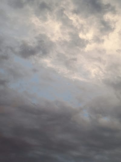 The image is a close-up, overhead view of a cloudy sky. The clouds are varied in color and texture, ranging from bright white and yellow near the top, to gray and dark gray lower down. There are hints of light blue sky visible between some of the clouds. The scene is devoid of any human presence or identifiable landmarks. The image appears to be a photograph of the sky taken from ground level, looking upwards. It is not possible to determine the specific location in Pankrushikha, Russia, from the image alone.