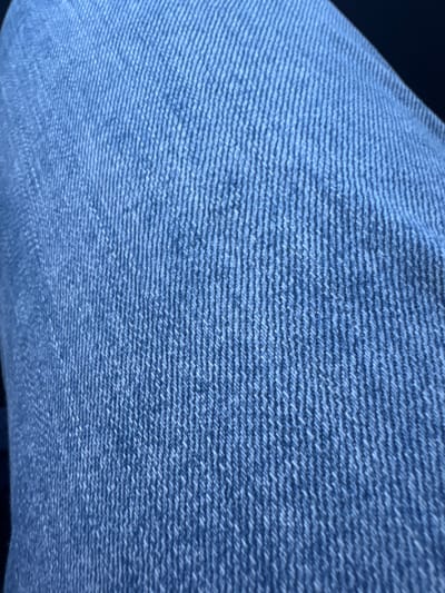 The image shows a close-up of blue denim fabric. The weave of the fabric is visible, with horizontal lines of the weft threads running across the image. The color of the denim is a medium blue with some lighter shades. The fabric appears slightly textured and soft. There is no indication of Strazha, Bulgaria, people, objects, or actions in this image.