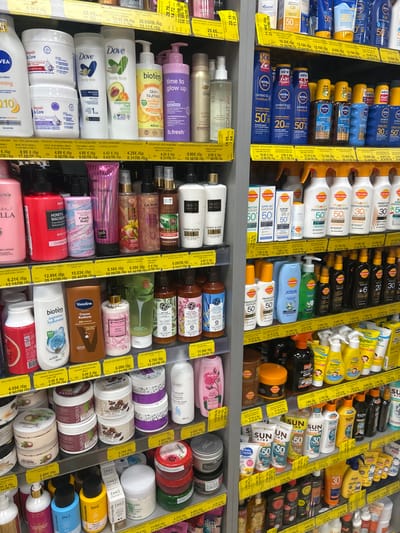 The image shows a well-lit, organized display of cosmetic and personal care products on multiple shelves in a retail setting. The products are predominantly sunscreens, lotions, body butters, and hair care items. Brands visible include NIVEA SUN, Dove, bioten, Victoria's Secret, Vaseline, and Carroten. Many products feature bright, colorful packaging, with a focus on sun protection with SPF indicated by numbers like 30 and 50. Prices are displayed on yellow tags in Bulgarian currency (лв, lev). The environment appears to be a supermarket or drugstore aisle, with no customers or staff visible. The shelving units are standard metal retail fixtures. The overall impression is one of a commercial display designed to attract consumers to a wide range of beauty and skincare products.