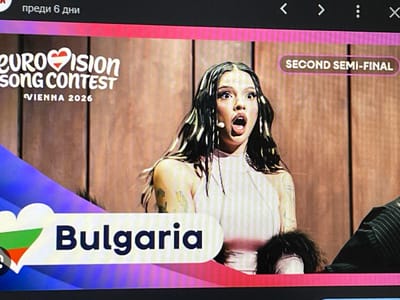 The image shows a screengrab of a television broadcast, possibly a YouTube video, featuring the Eurovision Song Contest. Text on screen indicates "Eurovision Song Contest, Vienna 2026, Second Semi-Final". The lower portion of the screen shows "Bulgaria" alongside a flag of Bulgaria within a heart shape. A woman with dark hair and blonde highlights is centrally featured with an open mouth. She is wearing a pale pink top. An individual in a dark pinstripe suit is visible on the right-hand side of the image. The background is a light brown wooden wall. The image appears to be captured from a television screen. There is no indication of the location being Nova Zagora, Bulgaria.
