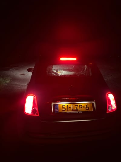 The image shows the rear of a dark-colored hatchback car at night. The car's taillights are illuminated, casting a red glow. The license plate of the car is visible, reading "51-LZP-6". There is a smaller text below the license plate which reads "REFA AUTOMOTIVE EDAM". The background is dark and appears to be an outdoor setting, possibly a road, with some reflections on the wet ground. There are no people visible in the image. The scene is forensic in nature, with no specific details suggesting a crime or unusual activity. The location is identified as Krautscheid, Germany.