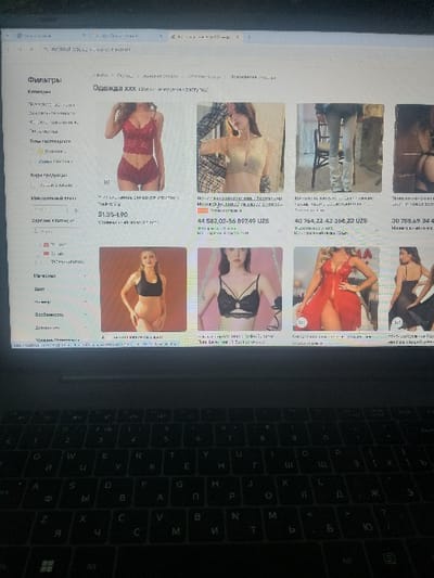 A laptop screen displays an online shopping page for lingerie. The page features various lingerie sets with prices listed in UZS. A menu on the left side includes filter options such as "Фильтры", "Тип", "Материал", and "Цвет", indicating search customization. The laptop's keyboard is visible on the right side of the screen, showcasing Cyrillic letters.