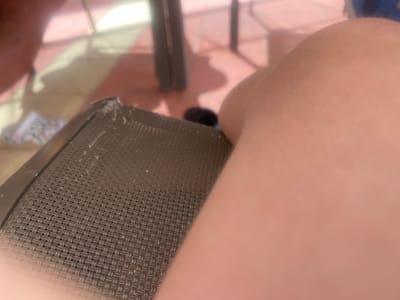 A close-up shot shows a person's leg resting on a brown wicker chair. Part of the leg is out of focus. A portion of a table leg is visible in the background. The setting appears to be outdoors, likely a patio or similar area. The location of the image is Monastir, Tunisia.