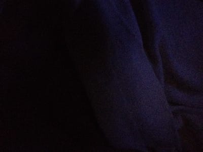 The image is a close-up, abstract shot of dark blue fabric. The fabric has a slightly textured appearance, with subtle variations in shade that suggest folds or creases. The lighting is dim, making it difficult to discern specific details. There are no people, animals, or discernible objects present in the image. The scene appears to be indoors due to the artificial lighting and the focus on the fabric. There is no visible indication of the location being in Sovetsk, Russia.