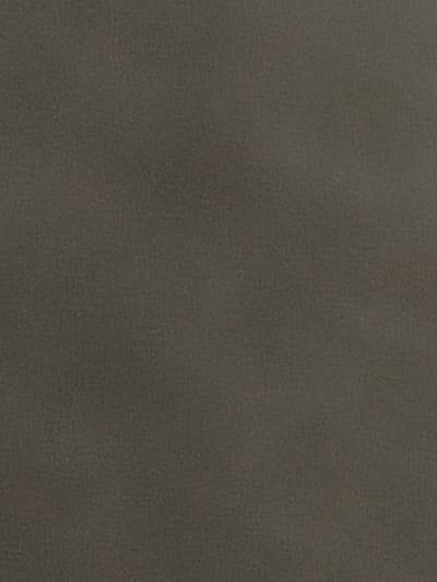 The image is a close-up, abstract shot of a textured surface, likely a fabric or a wall. The color is a uniform, muted gray with subtle variations in tone that suggest a granular or slightly mottled texture. There are no discernible objects, people, or environmental features visible in the image. The lighting appears diffuse and even, casting no distinct shadows.