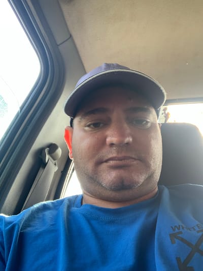 A man wearing a blue "OFF WHITE" branded t-shirt and a cap is inside a vehicle. A seat belt is visible. The location is unknown, and there is no information to suggest it is in Zetiovo, Bulgaria.