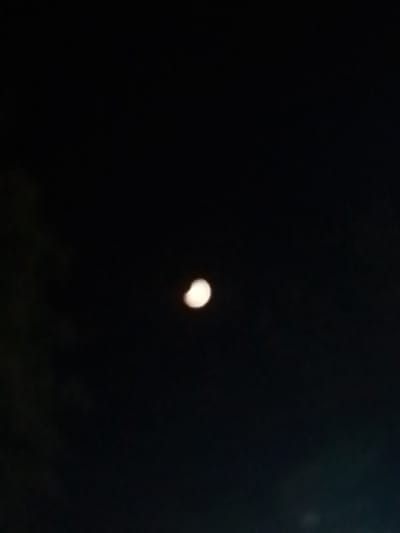 The image shows a dimly lit night sky with a crescent moon visible. The moon is partially obscured, suggesting it might be during a lunar eclipse or simply the phase of the moon. The sky is dark and appears to be free of clouds. There are no identifiable landmarks or people in the image. The setting is likely outdoors, given the view of the night sky. It is not possible to determine the specific location within Bukhara, Uzbekistan, from the provided image alone.