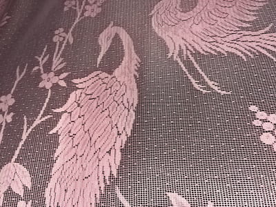 This media file shows a close-up view of a pink lace fabric with a pattern of cranes and floral elements. The lace is semi-transparent, with a fine mesh grid visible throughout. The pattern is detailed, featuring stylized depictions of cranes in flight and delicate floral motifs. The lighting suggests an indoor setting, possibly a home or a shop, with the fabric appearing to be illuminated from the front. The overall impression is one of delicate craftsmanship and decorative artistry.