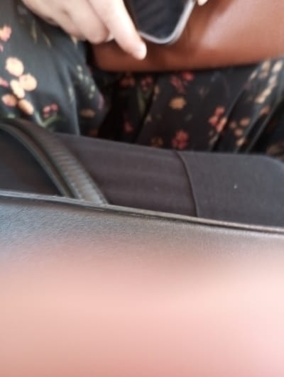 A person wearing a black floral patterned shirt with orange accents appears to be in transit, as evidenced by the dark gray or black seat in the foreground. The individual is holding a dark-colored object, possibly a phone or wallet, with their left hand. The scene lacks clear context and details to establish its location as Pyatiletka, Russia, or any other specific geographic location.