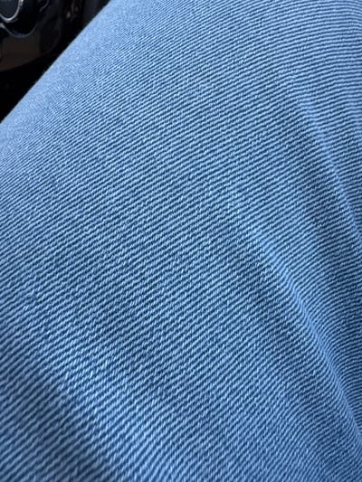 The image shows a close-up view of blue denim fabric. The texture of the denim is clearly visible, with the characteristic diagonal twill weave. The lighting suggests that the fabric is in a natural setting, possibly outdoors, as evidenced by the subtle variations in light and shadow across the surface. There are no people or discernible objects in the immediate foreground or background, focusing solely on the material itself. The location in Ghidighici, Moldova, is not visually identifiable from the provided image.