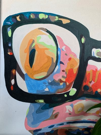 The image is a close-up, abstract painting on canvas, featuring bold, geometric shapes and vibrant colors. The central focus appears to be a stylized eye, rendered in shades of orange, yellow, and green, set within a black frame that suggests eyeglasses or goggles. Surrounding this central element are areas of pink, blue, and red, broken into smaller, distinct color blocks. The painting has a textured appearance due to the visible canvas weave and the application of paint. No specific location in Pisochyn, Ukraine, is depicted or implied by the image itself. The scene is purely artistic and does not represent a real-world environment.