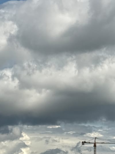 The image depicts a cloudy sky above the city of Pushkino, Russia. A construction crane is visible in the lower right corner of the frame. The clouds are predominantly gray, with some lighter white patches, suggesting overcast conditions. The scene appears to be a typical urban landscape with ongoing construction. There are no people or specific actions depicted in the image.