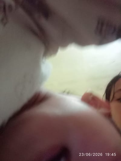 The image appears to be a low-resolution, out-of-focus snapshot taken from a very close perspective, possibly a selfie. The foreground is dominated by blurred flesh tones, suggesting a human body part, possibly a face or torso, is extremely close to the camera. To the right, a portion of a person's face is visible, with dark hair and an eye. The background is a washed-out, pale yellow or green, with some indistinct shapes that could be furniture or environmental features. In the bottom right corner, a timestamp reads "23/06/2026 19:45". The image quality makes it impossible to determine the specific location within Sukaraja, Indonesia, or any specific actions or interactions.