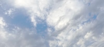 The image is a wide-angle, low-angle shot of a sky filled with scattered clouds. Patches of blue sky are visible through the clouds. The lighting suggests it is daytime, possibly late afternoon, with the sun partially obscured by clouds. There are no people, buildings, or other discernable objects in the frame, only the natural sky. The scene is consistent with an outdoor view from Fergana City, Uzbekistan, but there are no specific landmarks to confirm this location.