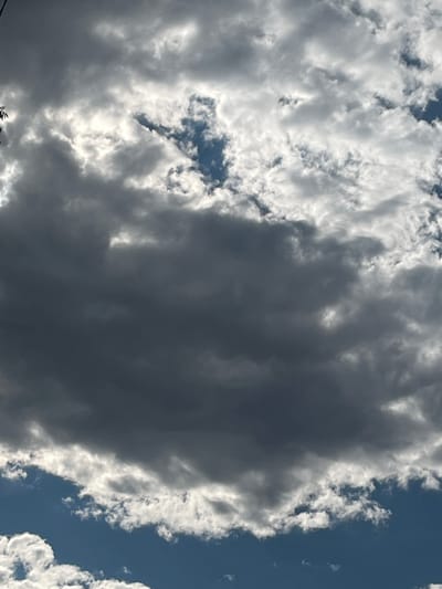 This media file captures a dramatic sky with a mix of dark, ominous storm clouds and bright, sunlit clouds. The scene is a wide-angle shot looking upwards, showcasing the dynamic interplay of light and shadow in the sky. A large, dark cloud formation dominates the center of the frame, casting a deep shadow. To the left and right, lighter, wispy clouds are illuminated by sunlight, creating a stark contrast. Patches of clear blue sky are visible through gaps in the clouds, particularly in the upper left portion of the image. The overall impression is one of a rapidly changing weather system, possibly a storm approaching or passing. The lighting suggests it is daytime, though the specific time is difficult to determine precisely due to the cloud cover. No people, objects, or specific location cues are visible beyond the sky itself. The weather appears to be unsettled, with a mix of sunshine and heavy cloud cover. The image evokes a sense of awe and perhaps a slight apprehension due to the presence of the dark storm clouds. There is no visible text in the image.