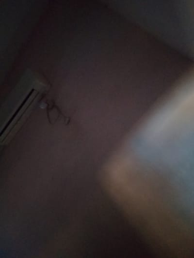 The image displays an interior scene, likely a room, with an air conditioning unit mounted on a wall. To the right of the air conditioning unit, a light fixture with exposed wires is visible. The lighting is dim, casting shadows and creating a washed-out effect on the right side of the image, suggesting a light source from that direction. The overall environment appears to be a residential or commercial space within Peshawar City Tehsil, Pakistan, given the context. No individuals are present in the frame.