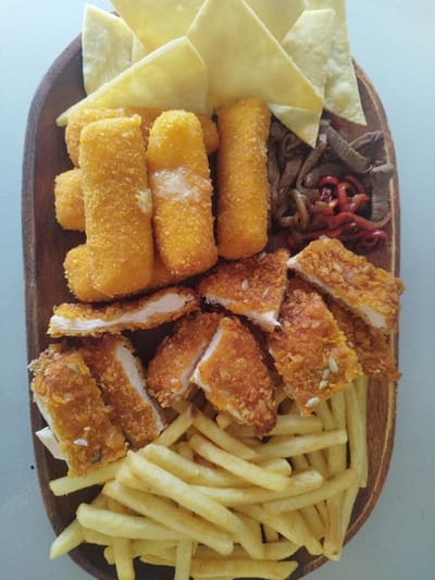 A wooden platter showcases a medley of fried delights. Golden tortilla chips sit atop a cluster of mozzarella sticks, some with melted cheese oozing. Thin slices of sauteed beef and red peppers accent the top right. Below, crispy chicken strips, cut into bite-sized pieces, rest above a pile of golden french fries. A textural and colorful assortment of fried foods.