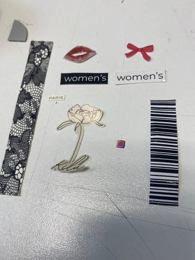 The image shows a collection of small cutouts and stickers arranged on a textured, light-colored surface, possibly a table or desk. The items appear to be decorative elements, perhaps part of a craft project or mood board.
Among the subjects are:
* A red ribbon tied in a bow.
* A pair of red lips.
* A stylized line drawing of a flower with a handwritten signature below it.
* A small square sticker with the Instagram logo, featuring a gradient of colors.
* A strip of black and white barcode.
* A strip of black lace pattern.
* A small gray, curved shape.
* Several text labels: "women's" (appearing twice, vertically on black backgrounds), and "PARIS" (horizontally on a white background).
The arrangement is haphazard, with items overlapping and scattered across the surface. There are visible scratch marks and a textured pattern on the surface itself. The lighting suggests an indoor environment, with no clear indicators of time of day or weather. The overall impression is one of assorted graphic elements laid out for creative assembly, without any specific scene or event depicted. The location context of Uchaly, Russia, is not visually evident from the image itself.