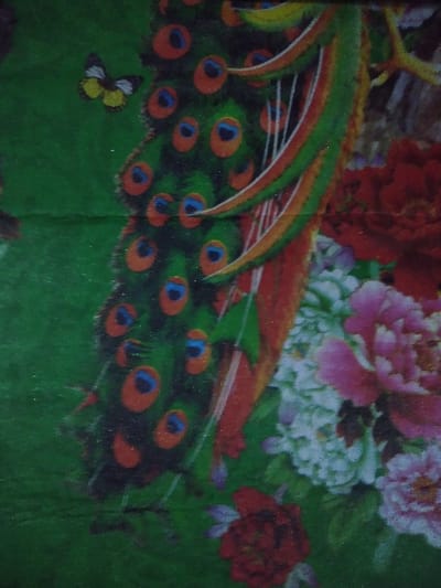 This image depicts a close-up of a flat, patterned surface, likely fabric or a print, and does not provide any discernible information regarding a specific location within Chimay, Belgium. The scene is static, featuring a vibrant, decorative motif.

The primary subject is a section of a peacock's tail, characterized by numerous green feathers each adorned with a distinct orange and blue ocellus (eyespots), originating from the right side of the frame and fanning towards the left. In the upper left quadrant, a yellow and dark-patterned butterfly is visible against the green background. The lower and mid-right portions of the image display a cluster of various floral elements, including prominent pink, white, and red blossoms. The background throughout the composition is a solid, uniform green, suggesting foliage or a stylized natural environment for the depicted flora and fauna. No people are present, and no actions or interactions are occurring.