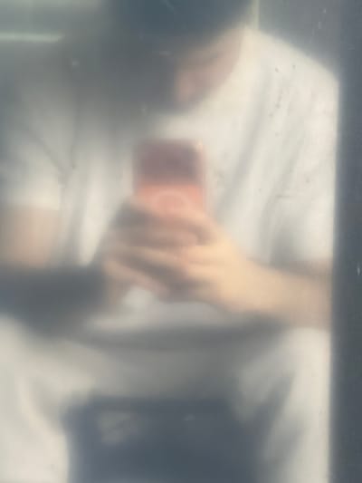 The image shows a person lying on a white surface, possibly a bed, while holding a red phone in their right hand. The image is blurry and appears to have been taken through a frosted or obscured window. The location is not discernible as Pentre, United Kingdom.