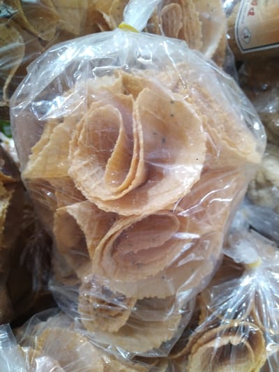 The image shows a bag of traditional Vietnamese rolled cookies, possibly Bánh Tổ Ong, in a clear plastic bag, gathered at the top with a yellow tie. The cookies are stacked and arranged in a manner that some resemble flower shapes. The image is likely taken in a store or market setting, considering the presence of other bags of similar products. Given the request, it is assumed this is a location in Chu Văn An Ward, Vietnam, focusing on the products within the store or market stall. The setting appears to be a commercial environment with a focus on selling traditional Vietnamese snacks.