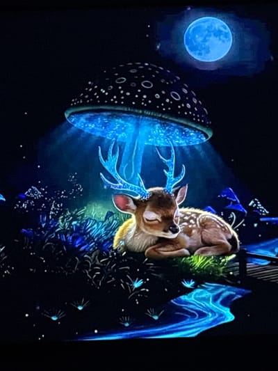 The image depicts a fictional, enchanting scene. In the foreground, a young deer with delicate antlers, illuminated by a soft blue light, rests peacefully amidst a lush, dark, and magical forest. Above the deer, a large, dark mushroom with white speckles emits a bright blue glow, casting an ethereal light on its surroundings. The forest floor is dotted with glowing blue flora and small, star-like lights, suggesting a nocturnal and mystical setting. In the upper right corner, a luminous blue full moon hangs in the dark sky, further enhancing the dreamlike atmosphere. The scene is entirely imaginary and does not correspond to any real-world location, including Skopje, North Macedonia.