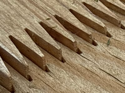The image shows a close-up, oblique view of a weathered wooden surface with parallel grooves. The wood appears to be rough-hewn or aged, with visible grain and some debris. The grooves are cut into the wood at an angle, creating a ridged pattern. Some small, light-green leaf fragments are present in some of the grooves. The lighting suggests an outdoor environment, possibly in a rural setting. The scene is devoid of any human presence or activity. The location, Гомельскі сельскі Савет, Belarus, is a rural administrative region.