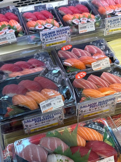 The image shows a display of pre-packaged sushi in clear plastic containers, likely in a supermarket or deli setting. The sushi types include salmon, tuna, and various combinations presented as "Salmon Maguro Dzukushi" and "Salmon Chutoro Nigiri." Prices are indicated in Indonesian Rupiah (Rp), ranging from Rp 71,000 to Rp 89,000. The packaging has branding from "Papaya Fresh Gallery," suggesting a specific store or chain. Text in Japanese is present. The image was likely taken in Medang, Indonesia, as the price tags indicate Indonesian currency.