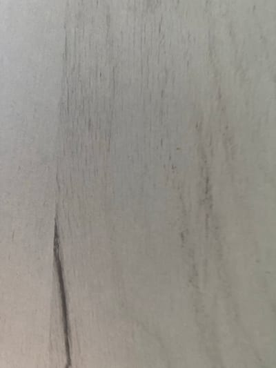 The image displays a close-up, vertically oriented view of a light gray, textured surface with subtle vertical striations and darker, irregular lines. The texture appears to be consistent with a wood-grain pattern or a similar natural material. There are no discernible objects, people, or actions within the frame. The lighting is soft and diffused, casting no harsh shadows. The overall impression is one of a plain, neutral background. Without additional context, it is impossible to determine the specific location within Uzhur, Russia.