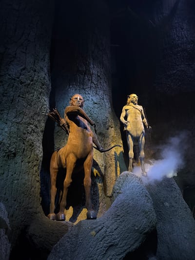 The image depicts two figures in a dark, cave-like setting. The upper figure is gray and appears to be emerging from a hole, with a plume of white smoke or vapor surrounding it. The lower figure is brown and appears to be embedded in a textured, rocky surface. Both figures are positioned horizontally. The environment consists of a rough, uneven surface resembling rock or cave walls. The lighting is dim, with focused illumination on the figures. The location is Nerima, Japan.